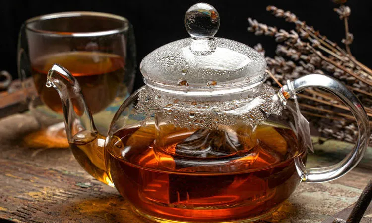 A steaming glass teapot and cup of tea.