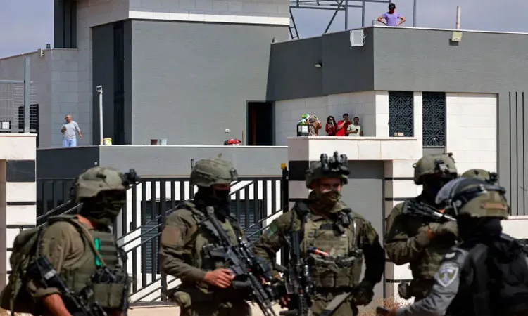 Israeli soldiers stand in front of the entrance of a besieged Palestinian house by Israeli settlers in the village of Qusra, south of Nablus, in the occupied West Bank